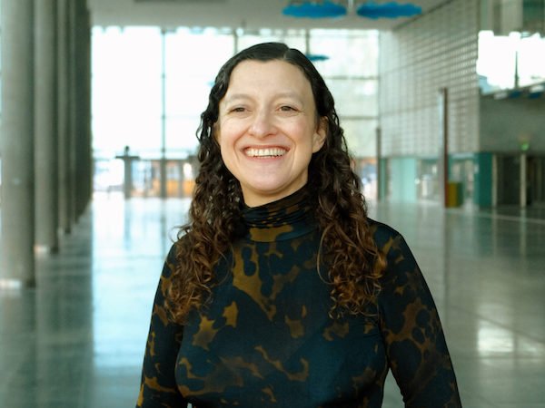 A white woman in a brown shirt standing in a convention hall.